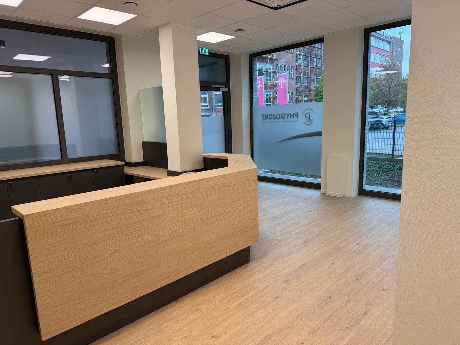Empfangsbereich mit Holztresen und großer Fensterfront mit PhysioZone-Logo